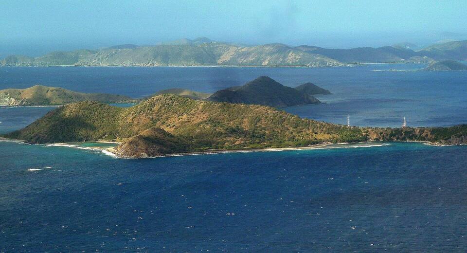 Cooper Island from the air, its green hills and sandy shore ringed by reef, with Salt Island and Peter Island beyond